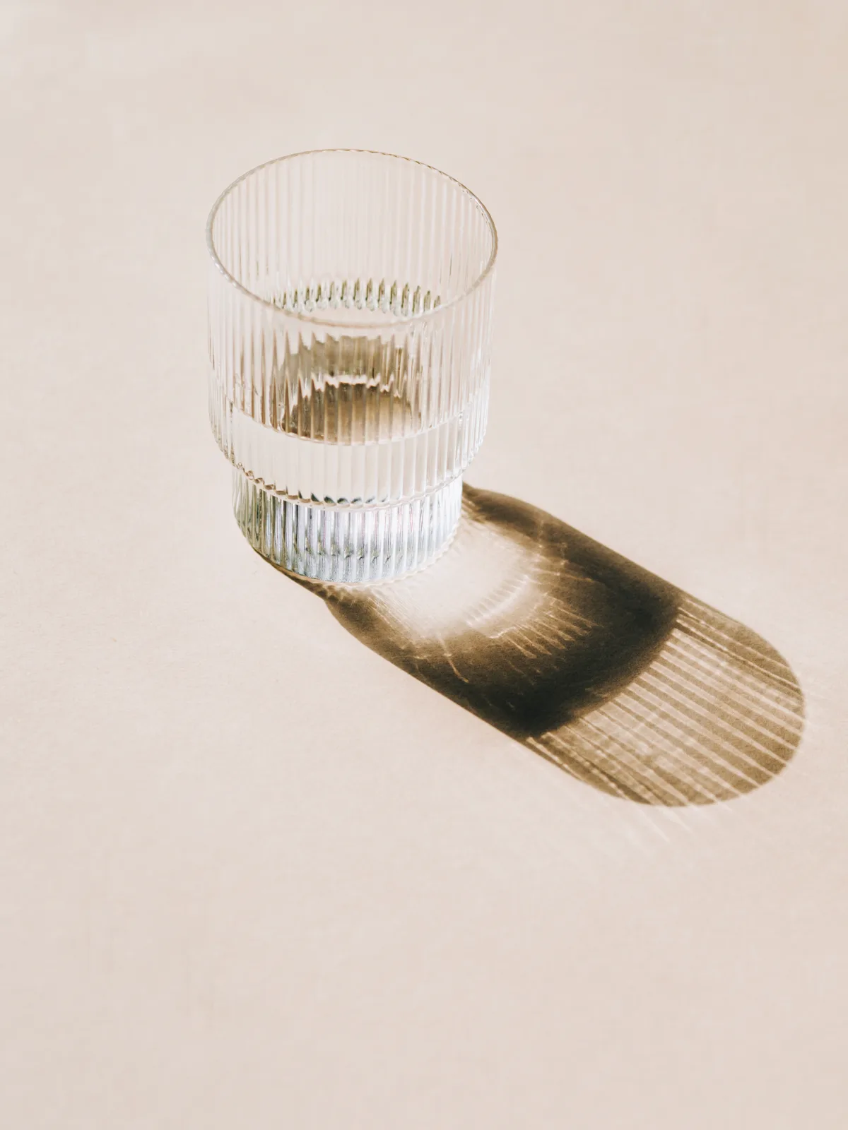 A glass of water casting a long shadow on a warm surface